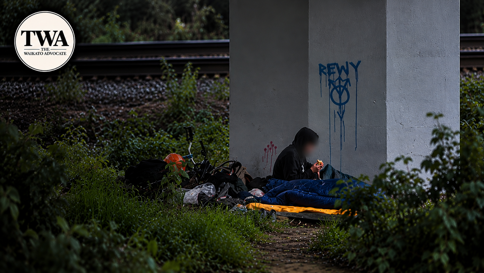 A person sheltering with their belongings beneath a bridge in the Waikato