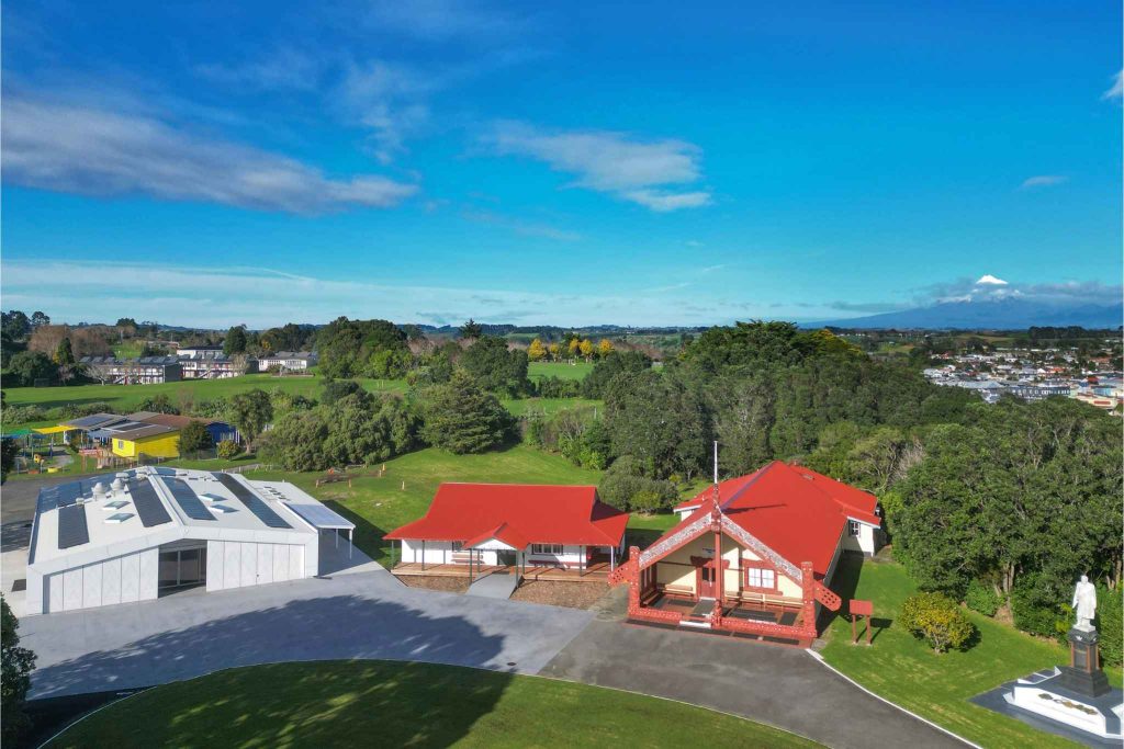 Aerial view of Ōwae Marae in Waitara showing the new building with rooftop solar panels, traditional marae buildings and Maunga Taranaki in the distance